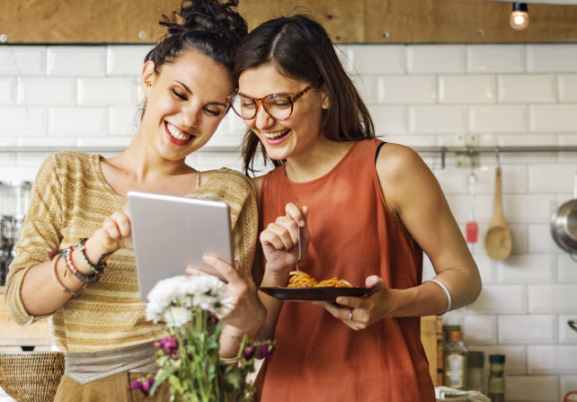 Two women look together at a tablet while sitting at a table.